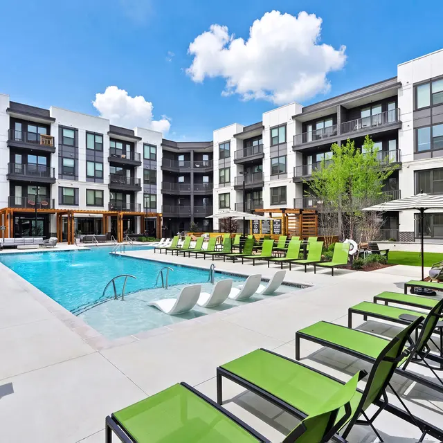 Community Pool Area in Modern Apartment Complex An outdoor pool area surrounded by modern apartment buildings, featuring lounge chairs and umbrellas under a clear blue sky.