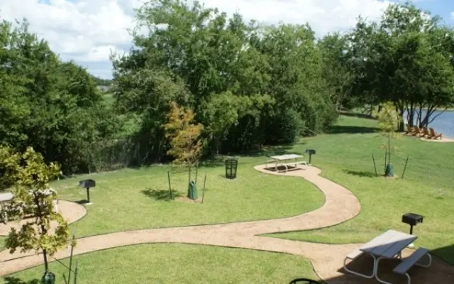 Outdoor Park Area A landscaped outdoor park area featuring picnic tables, winding paths, and trees, set against a backdrop of blue skies and greenery.