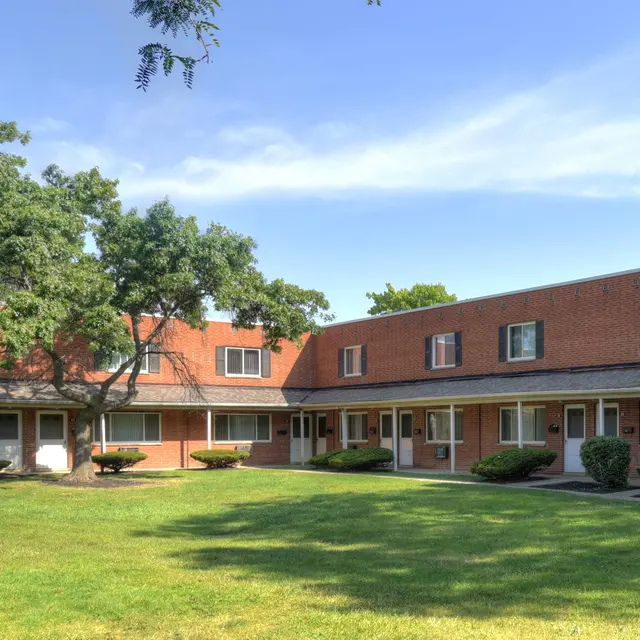 A view of a brick apartment complex surrounded by well-maintained grass and trees under a clear blue sky.