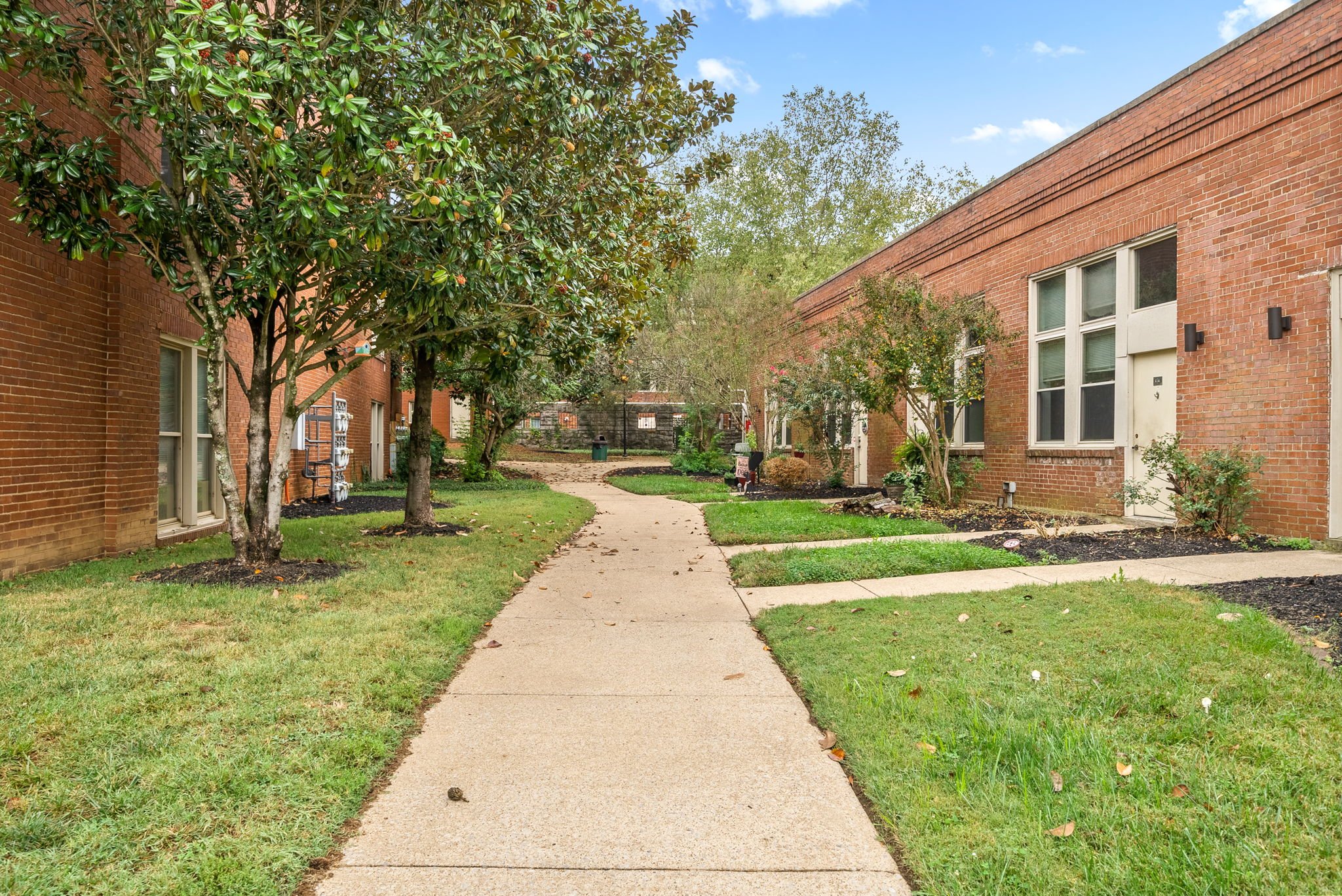 Residential Pathway in a Park-like Setting A calm residential pathway flanked by brick buildings and greenery, with a clear blue sky overhead.