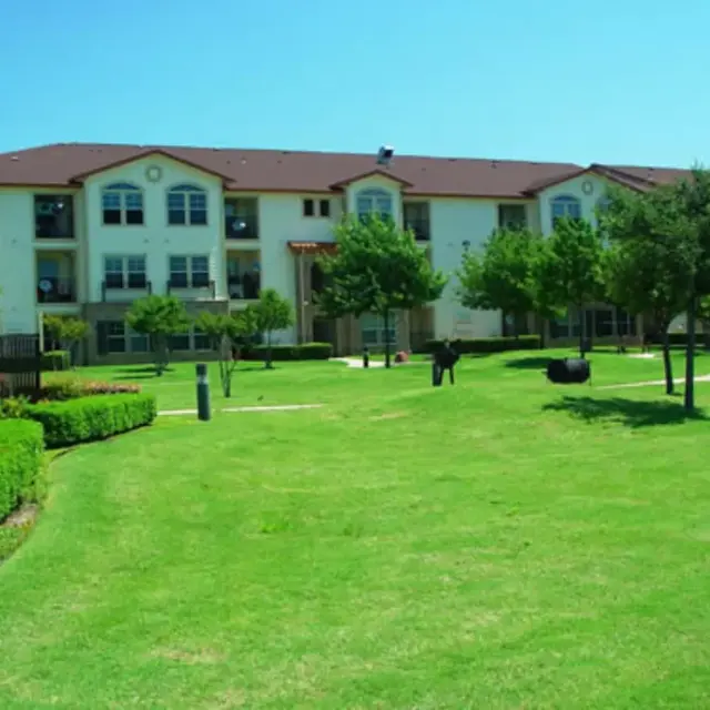 Apartment Complex with Green Space A well-maintained apartment complex with three stories, surrounded by green lawns and trees.