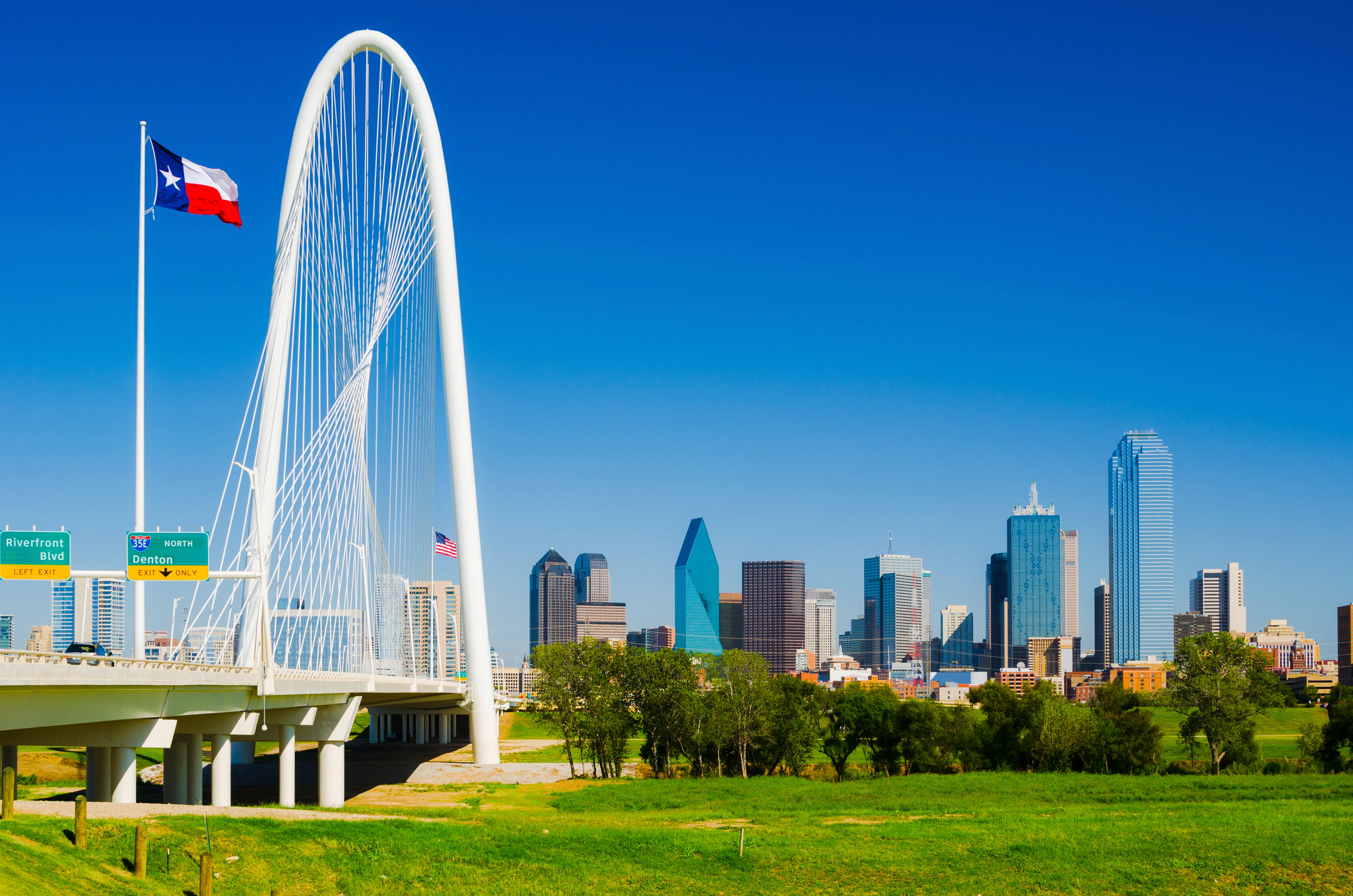 Dallas skyline featuring a modern cable-stayed bridge and Texas flag in clear blue sky