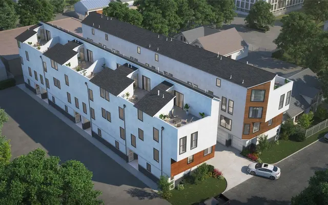 An aerial view of a modern apartment building featuring white and wooden facades, with several balconies, surrounded by trees and parked cars.