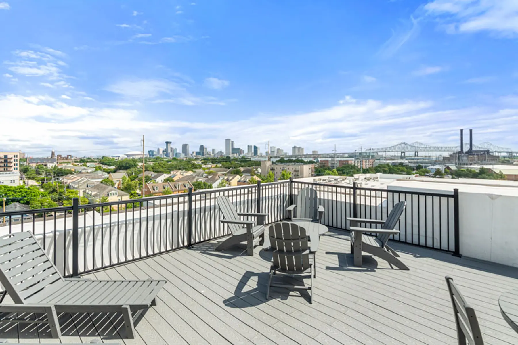 A spacious rooftop terrace with wooden lounge chairs and a view of a city skyline under a bright blue sky.