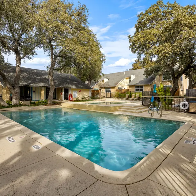 A swimming pool surrounded by trees and residential buildings, featuring clear blue water and lounge chairs.