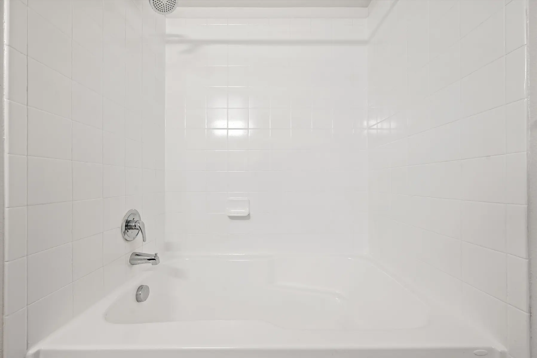 A clean and simple bathroom featuring a white bathtub and tiled walls.