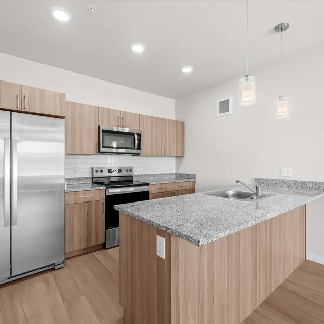 A modern kitchen featuring wooden cabinetry, stainless steel appliances, and a large island with a granite countertop.