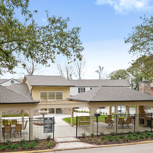 An outdoor community area featuring two gazebos with seating, surrounded by lush greenery and residential buildings in the background.