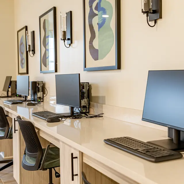 A modern workspace featuring several desktop computers with ergonomic chairs, situated in a brightly lit room adorned with abstract artwork on the walls.