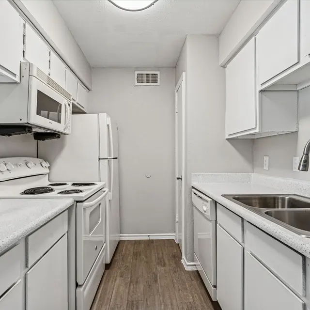 Bright and modern kitchen featuring white cabinets, countertops, and appliances, with wooden flooring and ample natural light.