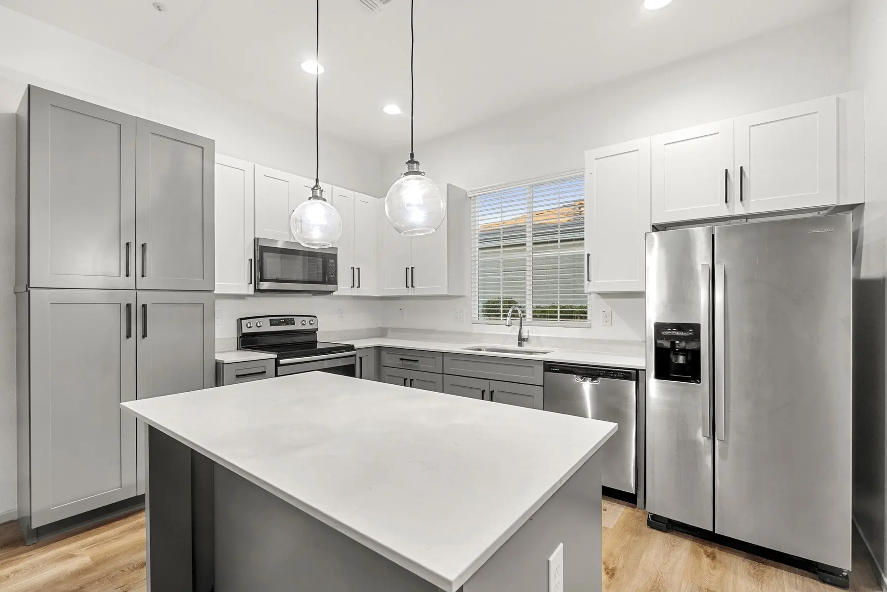 Modern kitchen with gray and white cabinetry, stainless steel appliances, and a large island with a white countertop.