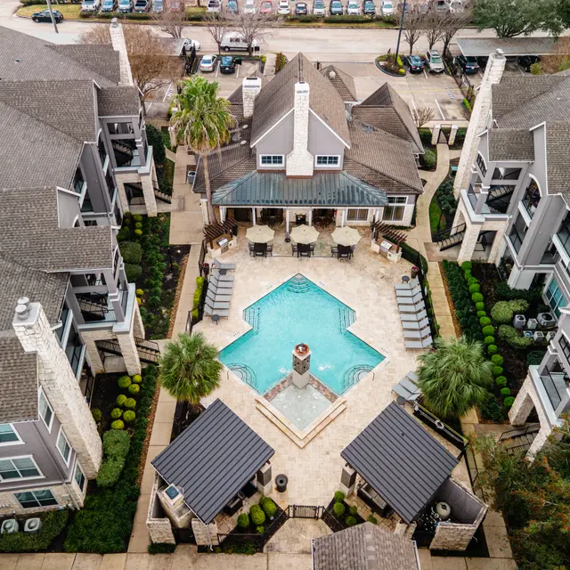 Aerial view of a modern apartment complex featuring a central pool area surrounded by greenery and lounge chairs.