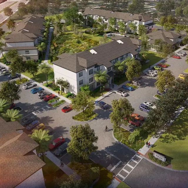 Aerial view of a new residential development featuring multiple buildings, parking spaces, and landscaped areas.