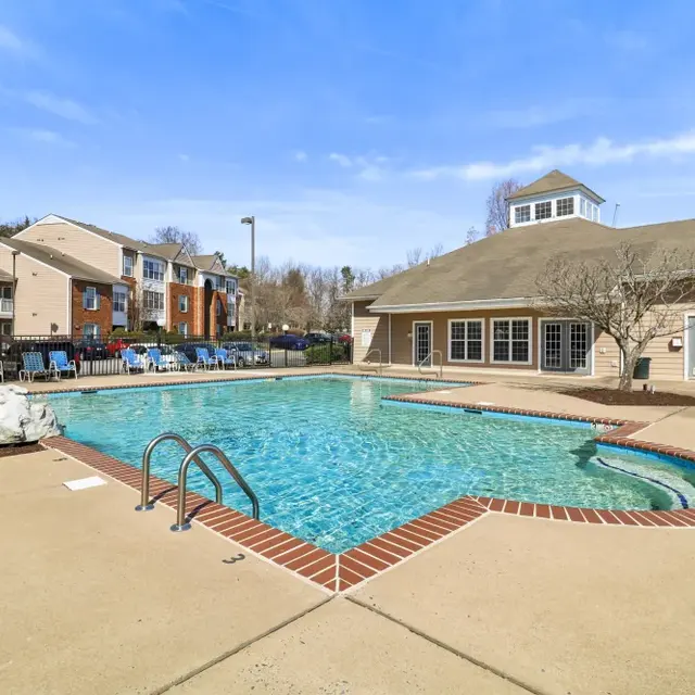 A spacious outdoor swimming pool area with lounge chairs around it, adjacent to a building with large windows.
