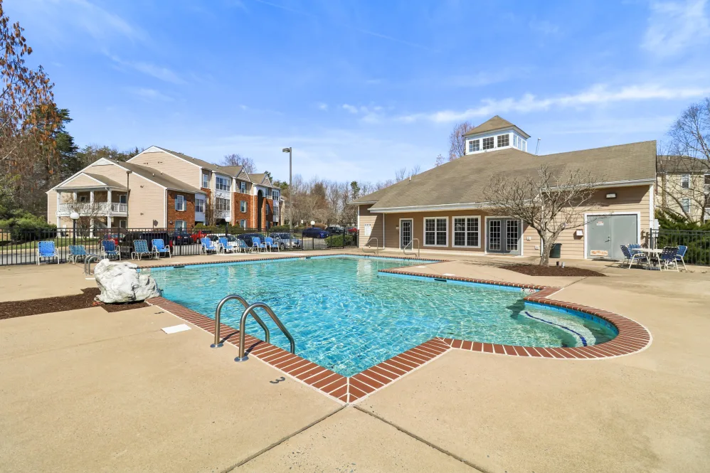 A spacious outdoor swimming pool area with lounge chairs around it, adjacent to a building with large windows.