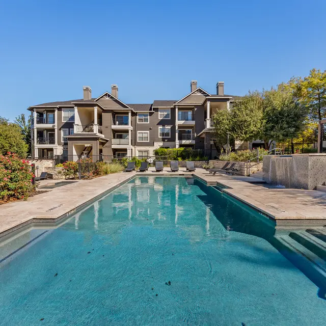 A serene pool area surrounded by landscaped gardens and apartment buildings under a clear blue sky.