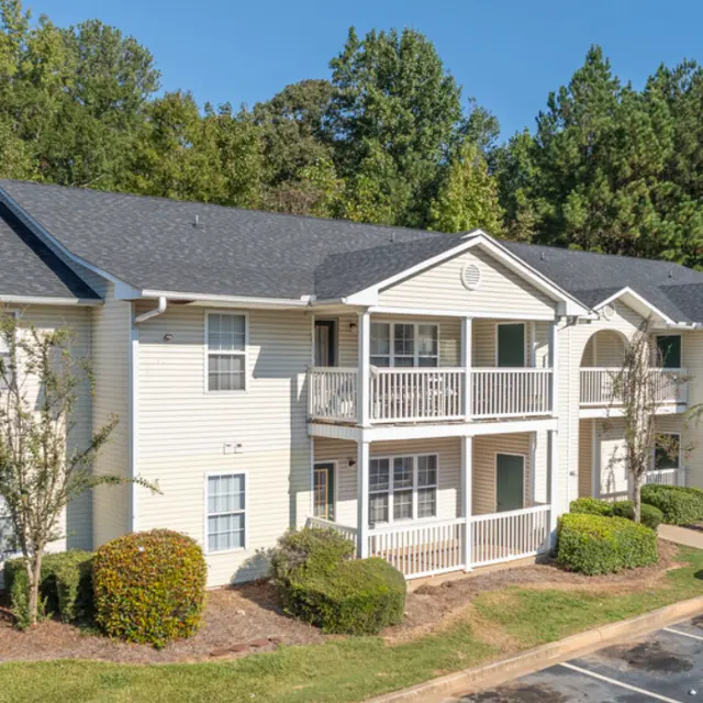 Exterior view of a two-story apartment complex surrounded by trees and a parking area.