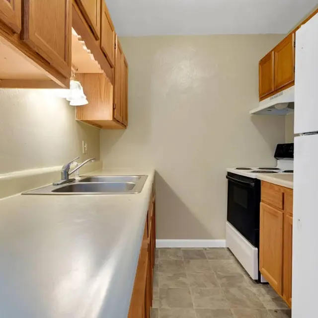 A small kitchen with wooden cabinets, a white stove, and a sink.