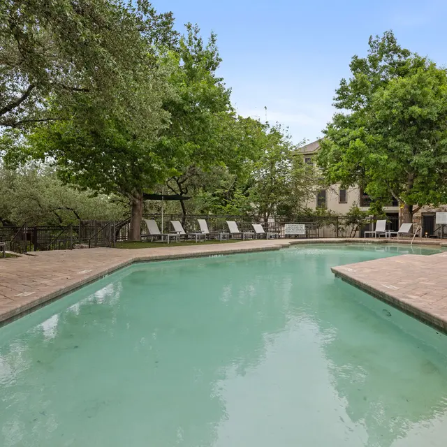 A serene swimming pool surrounded by green trees and lounge chairs in a residential area.