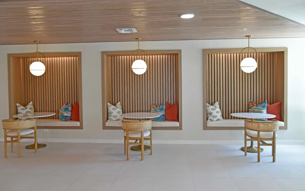 A spacious and modern interior featuring three seating alcoves with cushioned benches and small round tables. Each alcove has warm wooden paneling and stylish circular pendant lights. Brightly colored cushions enhance the inviting atmosphere.