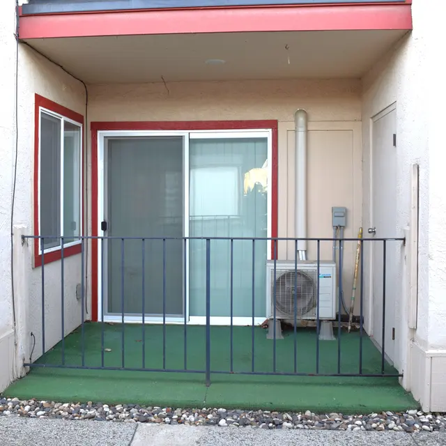 Apartment Balcony View A small balcony with a green floor mat and black railing leading to sliding glass doors, accompanied by an air conditioning unit.