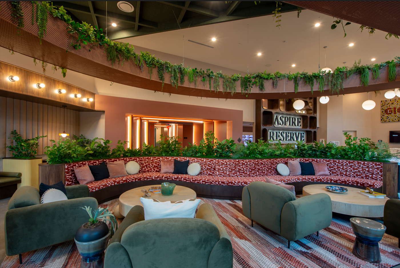 Contemporary Community Lounge A spacious community lounge with a curved seating arrangement surrounded by greenery, featuring decorative plants, contemporary furnishings, and warm lighting.