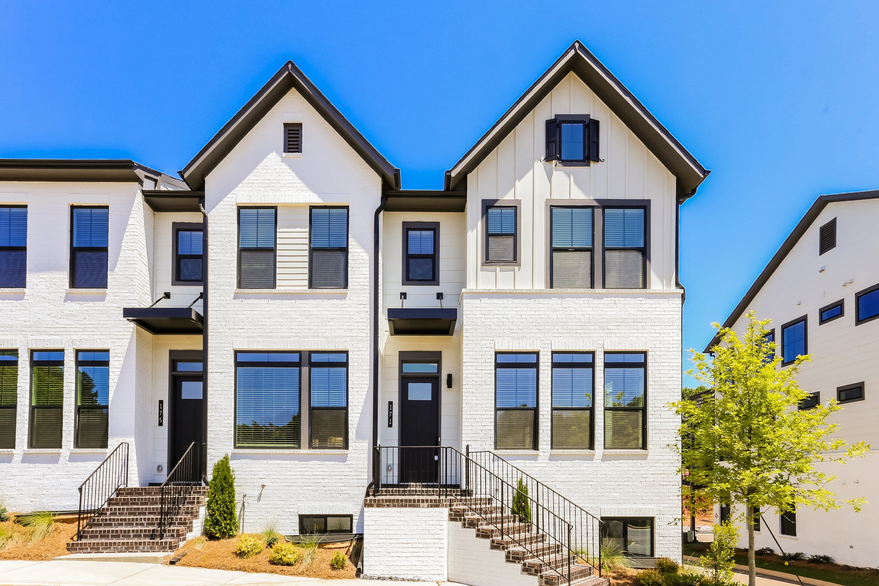 A row of modern townhouses with white brick exteriors and black accents under a clear blue sky.