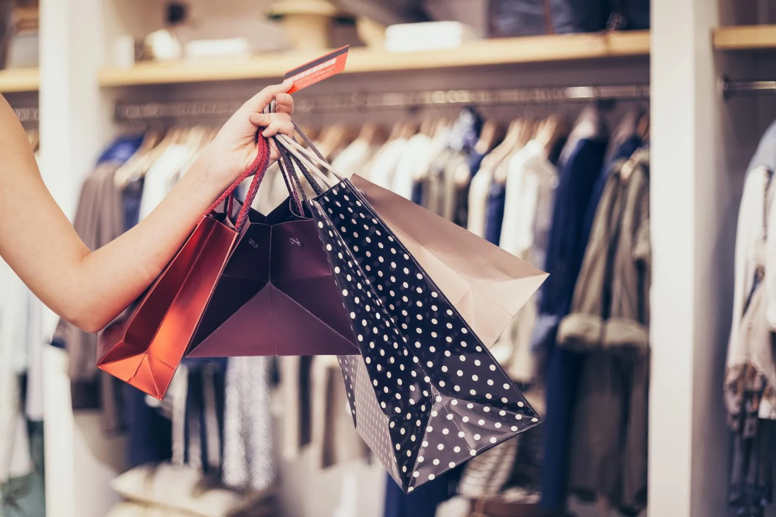 A person's hand holding multiple shopping bags in a clothing store.
