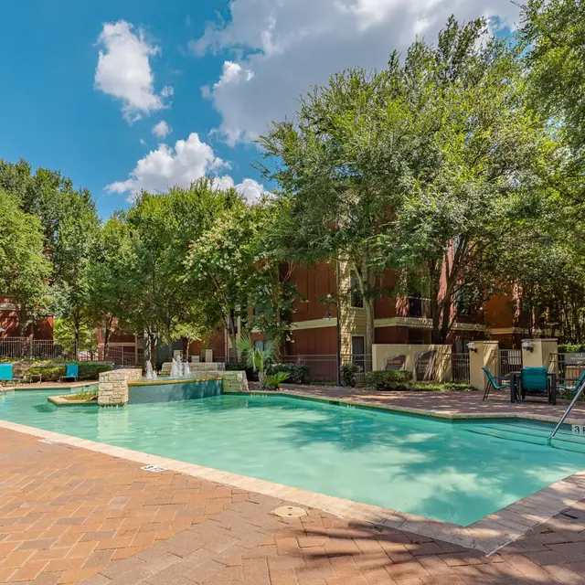 Outdoor Swimming Pool Area A vibrant swimming pool area surrounded by lush green trees and blue sky with fluffy clouds.