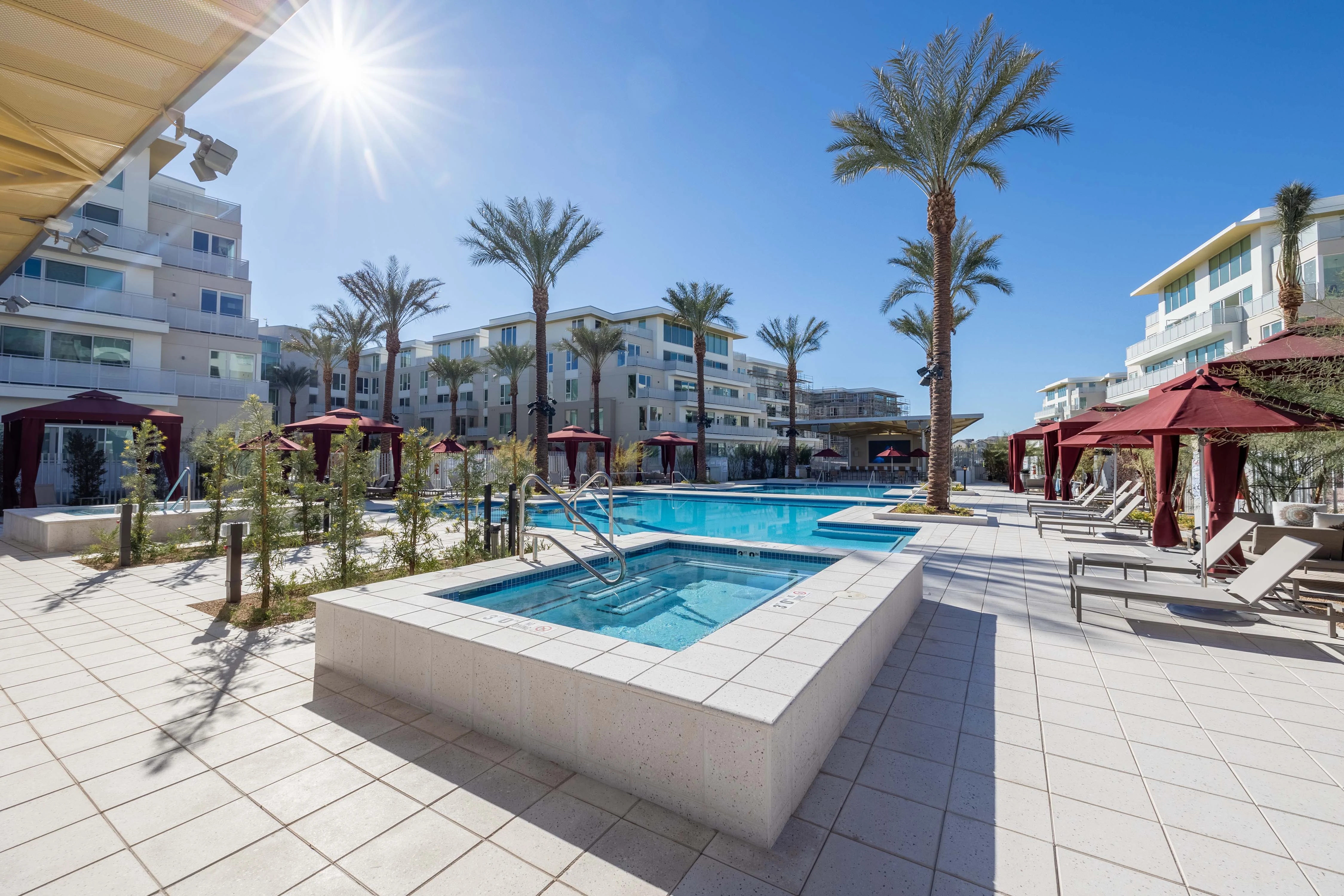 A spacious pool area in a luxury apartment complex with palm trees and lounge chairs.
