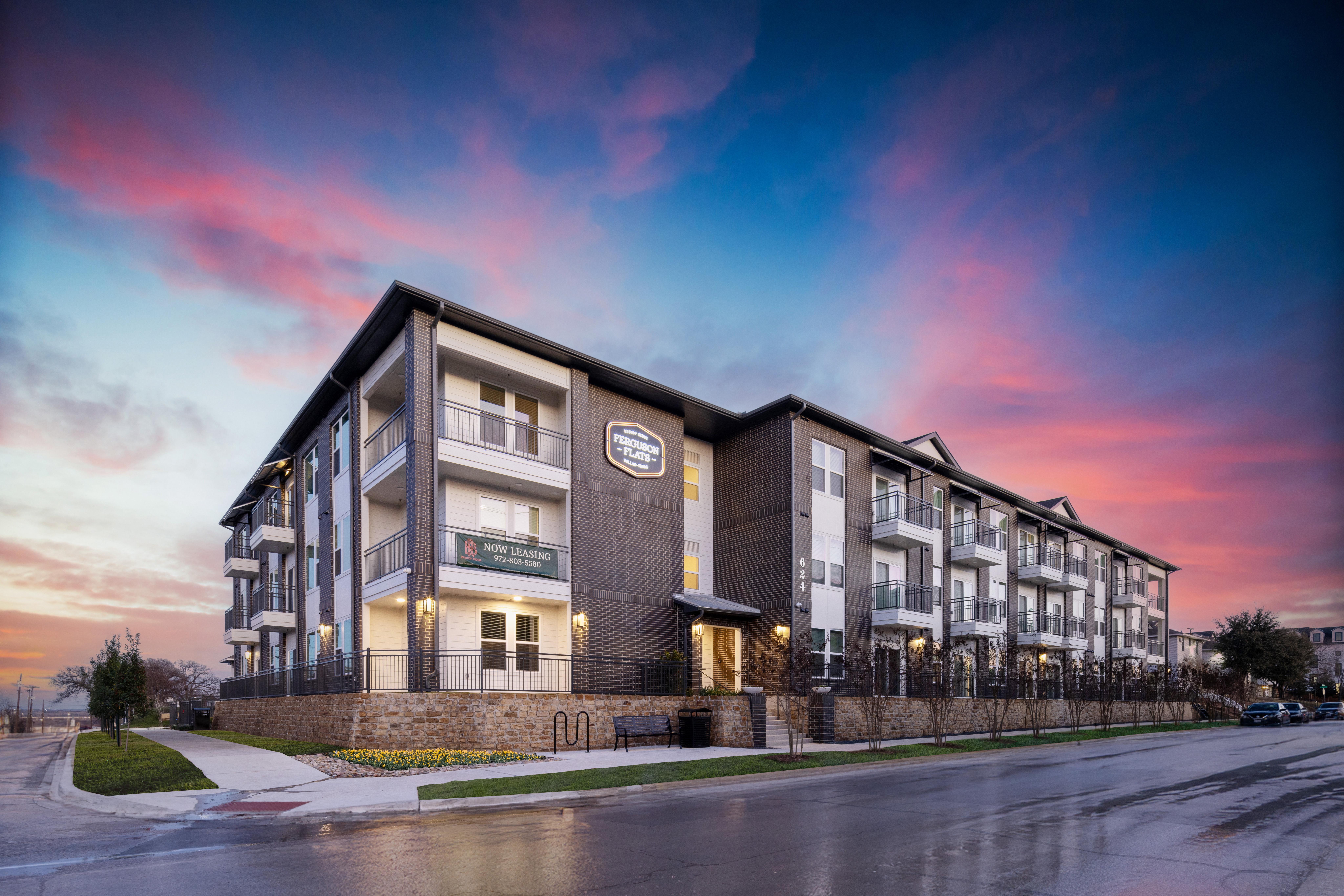 A modern apartment building with balconies under a colorful sunset sky.