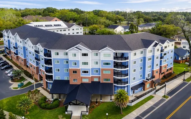 A multi-story commercial building with a colorful exterior featuring blue and orange hues, surrounded by green landscaping and a paved road.