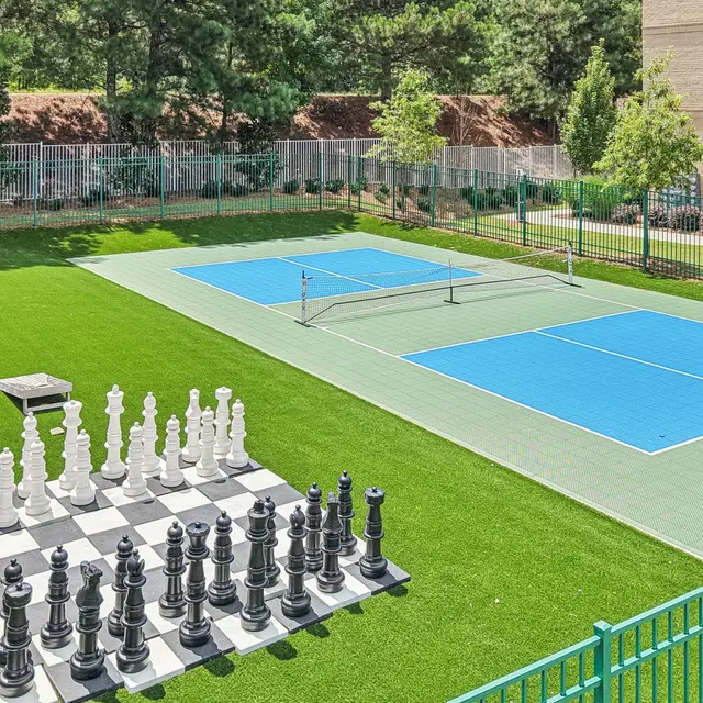 Outdoor Chess and Tennis Courts An outdoor area featuring a large chess set and two blue tennis courts on artificial grass.