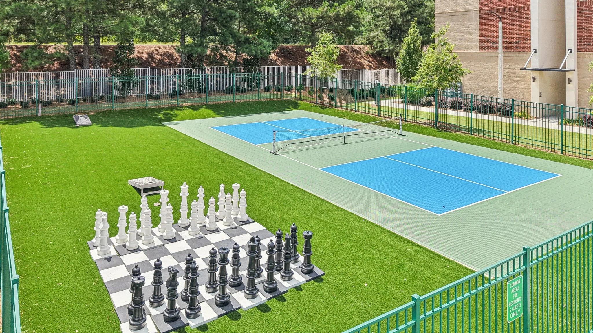 An outdoor area featuring a large chess set and two blue tennis courts on artificial grass.