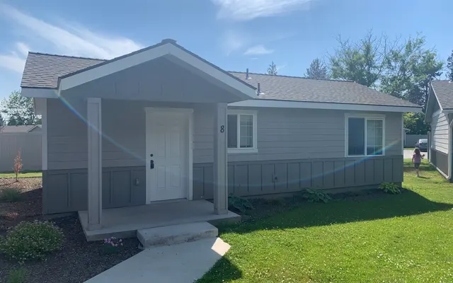 Charming Single-Story Home A single story house with a gray exterior, a white front door, and green lawn.