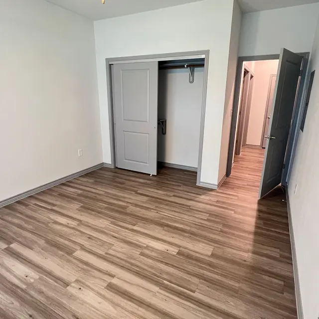 An empty room featuring light wood flooring, a ceiling fan, and two sets of gray doors leading to closets.