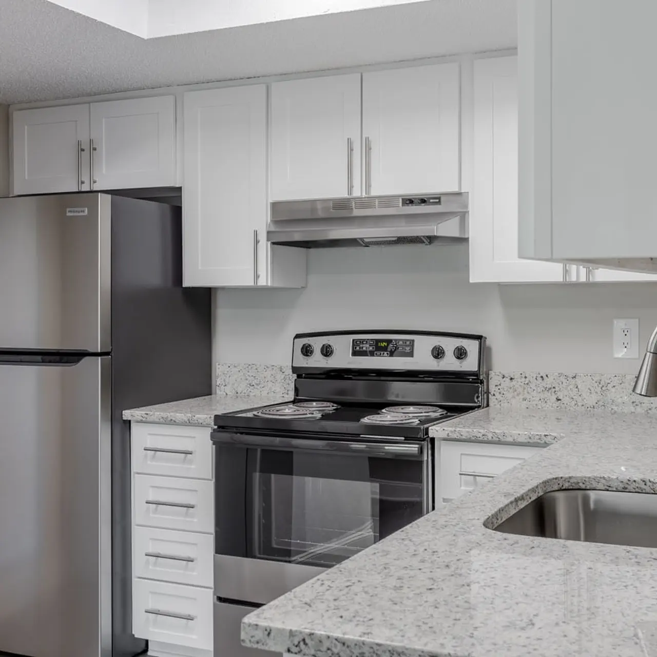 A modern kitchen featuring stainless steel appliances, white cabinets, and granite countertops.