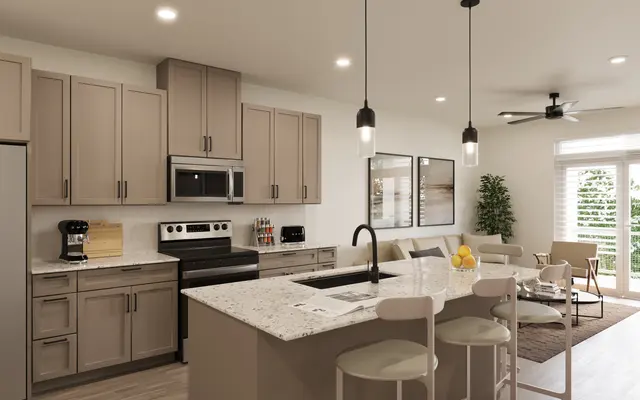 A modern kitchen with light cabinets, granite countertops, and stainless steel appliances, connected to a cozy living room featuring a couch and coffee table.