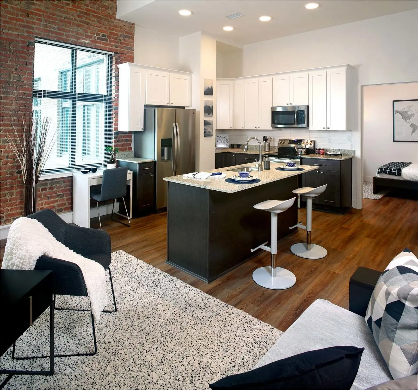 A modern apartment interior featuring a kitchen island, dining area, and living space with a mix of brick and white cabinetry.