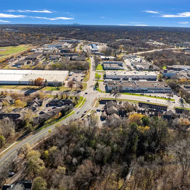 Aerial view of a suburban area with residential homes, roads, and commercial buildings surrounded by greenery and open fields.