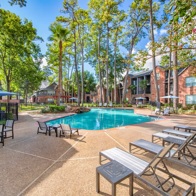 A sunny view of a landscaped pool area surrounded by residential buildings, featuring lounge chairs and umbrellas.