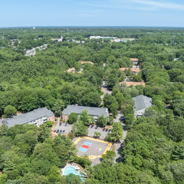 Aerial View of Residential Neighborhood Aerial view of a lush, green residential neighborhood featuring multiple buildings surrounded by trees, with a multicolored playground in the center.