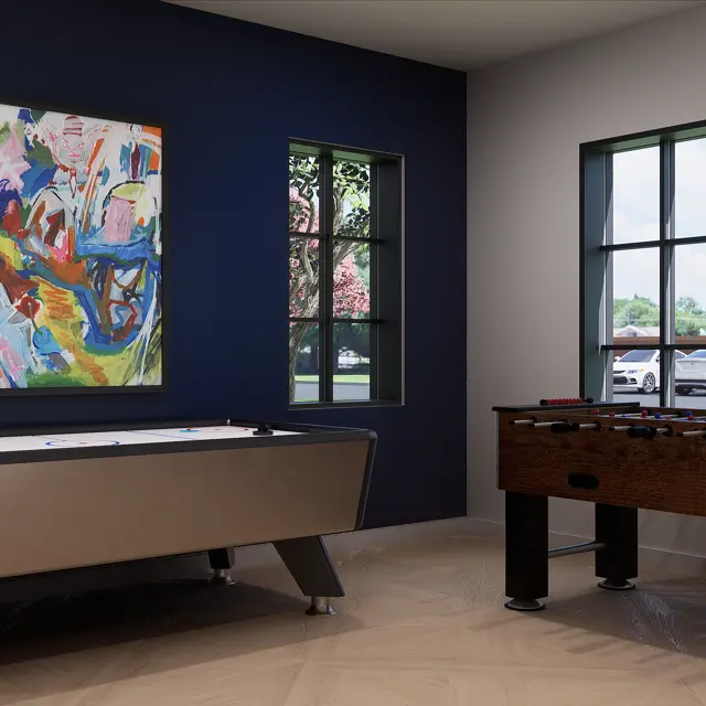 A modern game room featuring a pool table and a foosball table, with large windows allowing natural light to fill the space. A vibrant abstract painting hangs on the wall beside the pool table.