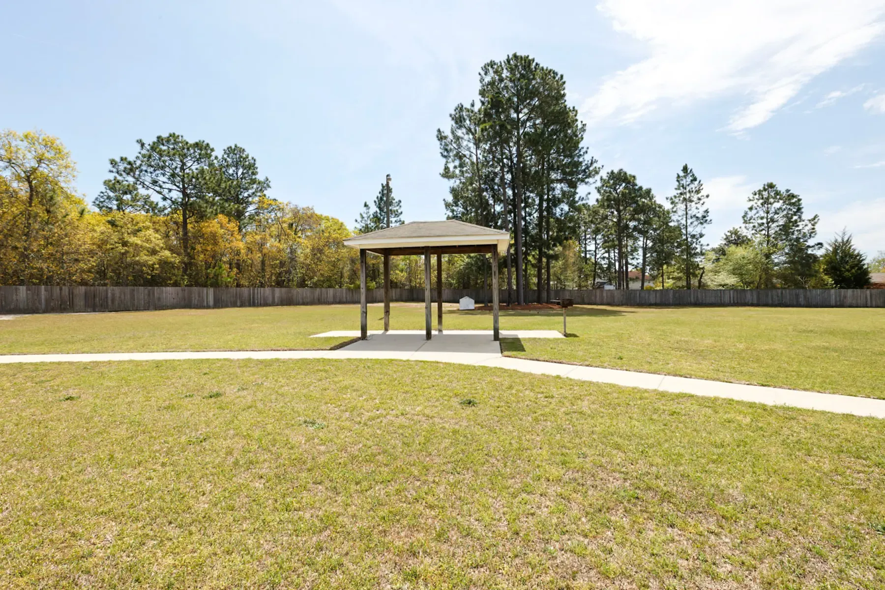 A spacious park with a wooden shelter in the center, surrounded by grass and trees against a clear blue sky.