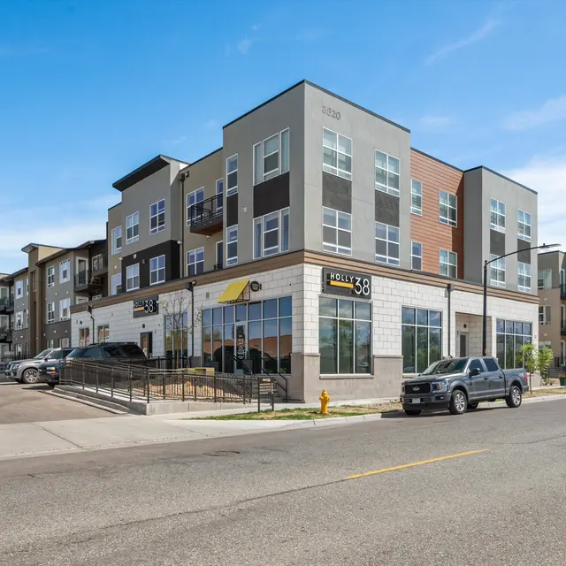 Modern apartment complex with multiple floors and balconies, situated on a corner street.