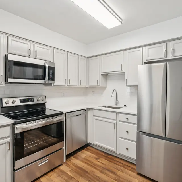 Modern Kitchen with Stainless Steel Appliances A modern kitchen featuring white cabinets, stainless steel appliances including a refrigerator, microwave, and oven. The countertop is white and the flooring is wood laminate.