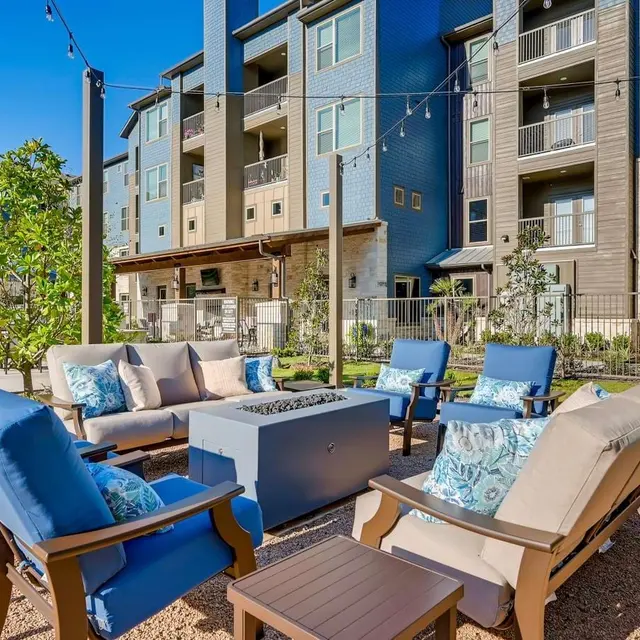 Outdoor lounge area with comfortable seating and a fire pit, surrounded by apartment buildings.