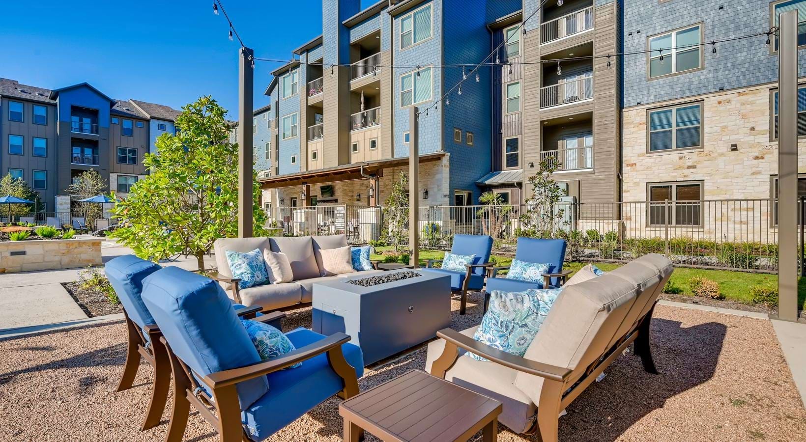 Outdoor lounge area with comfortable seating and a fire pit, surrounded by apartment buildings.