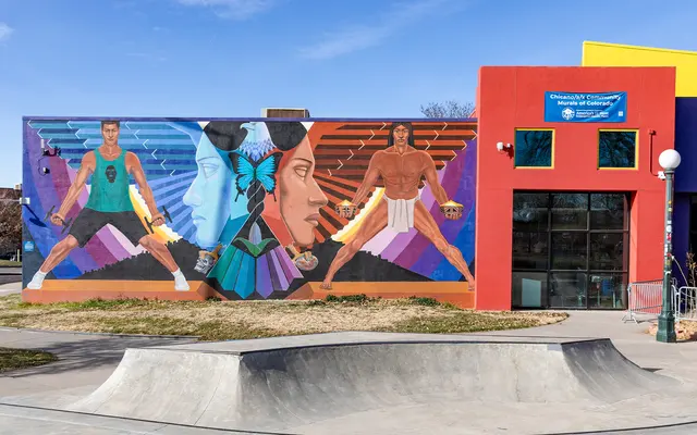 CELEBRATING HISTORY A vibrant mural on a building featuring four figures representing different cultures and backgrounds. The characters are depicted in dynamic poses, showcasing their ethnicity and strength, with a colorful background and geometric patterns. Skatepark in the foreground.