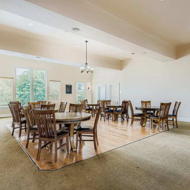Spacious Community Meeting Room A spacious community meeting room featuring several round tables with wooden chairs arranged in a U-shape. Large windows let in natural light, and there are two small meeting rooms visible in the background.